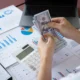 Business owner counting money over financial reports and charts representing cash flow management and business profitability.